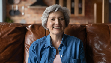 Image of smiling older woman sitting on a leather couch.